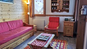 A cozy room with a wooden sofa, a red armchair, a small table with a tray, and a cabinet with kitchen items.