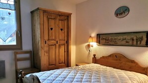 A bedroom with a bed, wooden wardrobe, and a wall-mounted lamp.