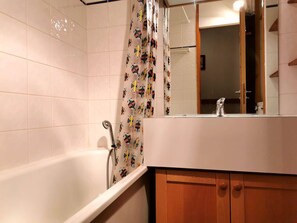 Ein Badezimmer mit Badewanne, einer Duschtasse mit farbigem Muster, einem Holzschrank und einem Spiegel über dem Waschbecken.