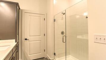 Un baño con cabina de ducha de vidrio, una puerta blanca y piso de baldosas.