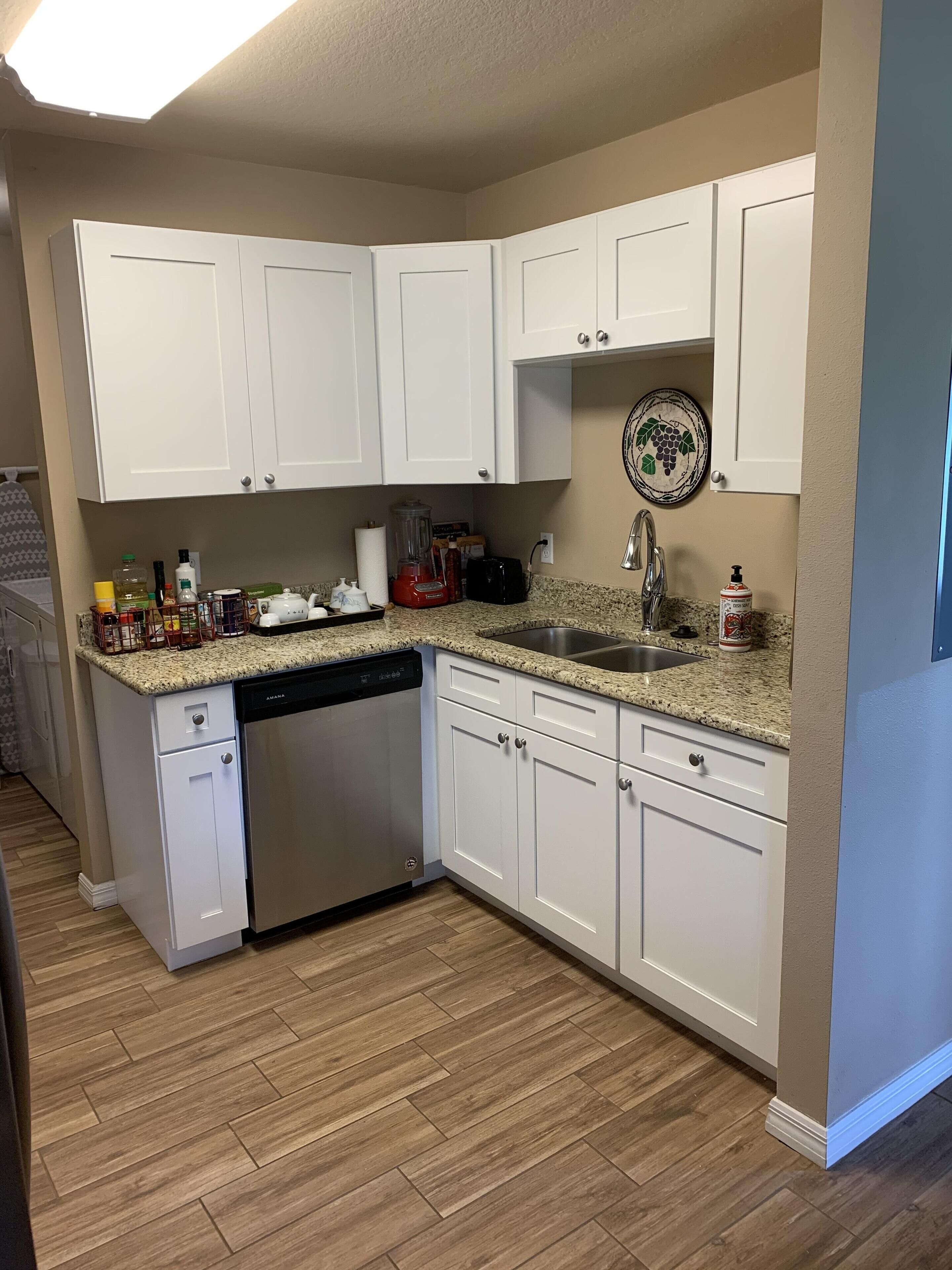 A kitchen with white cabinets, a granite countertop, a dishwasher, and a sink.