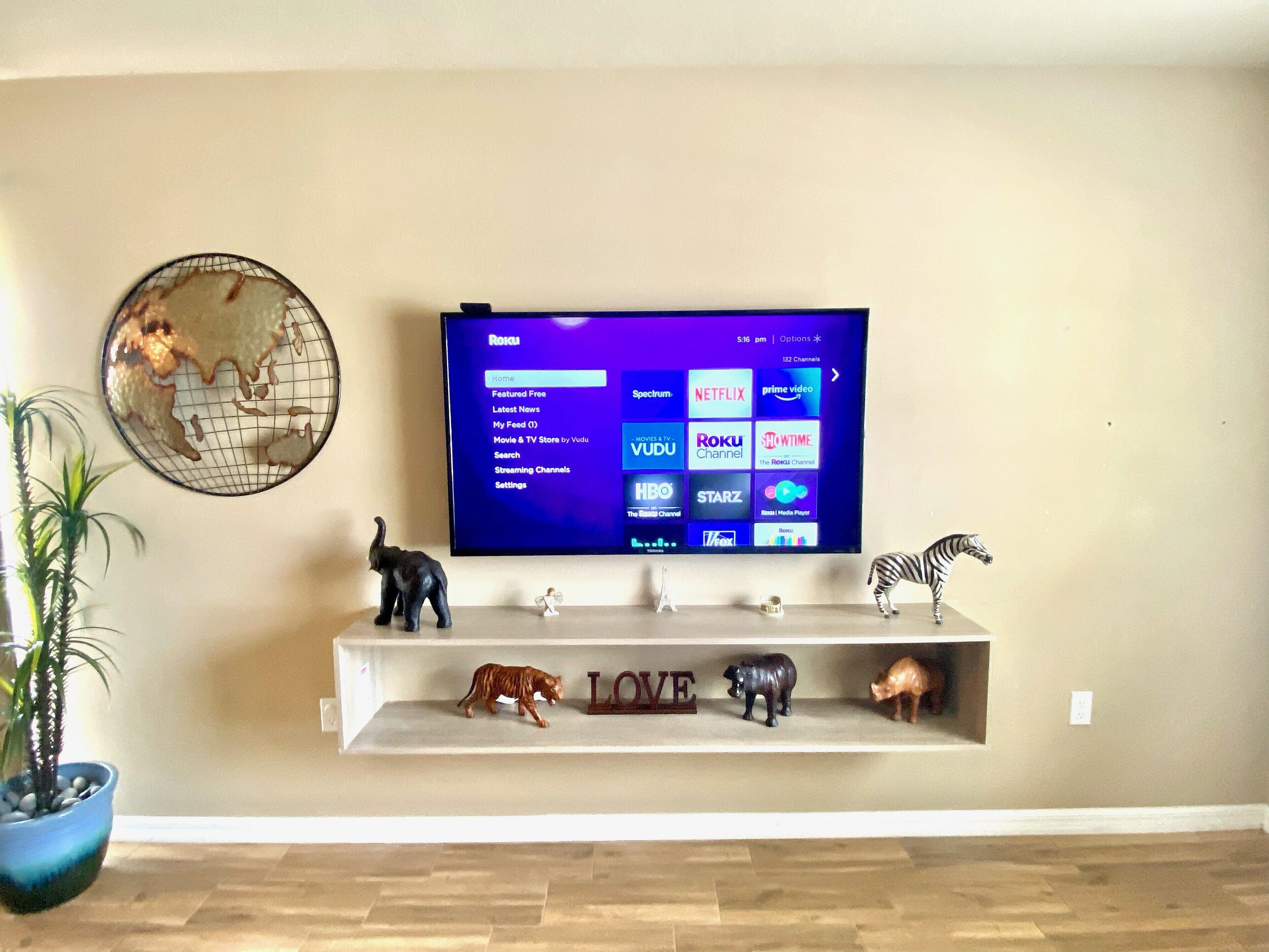 A flat-screen TV mounted on a wall with a shelf below displaying animal figurines and a globe.