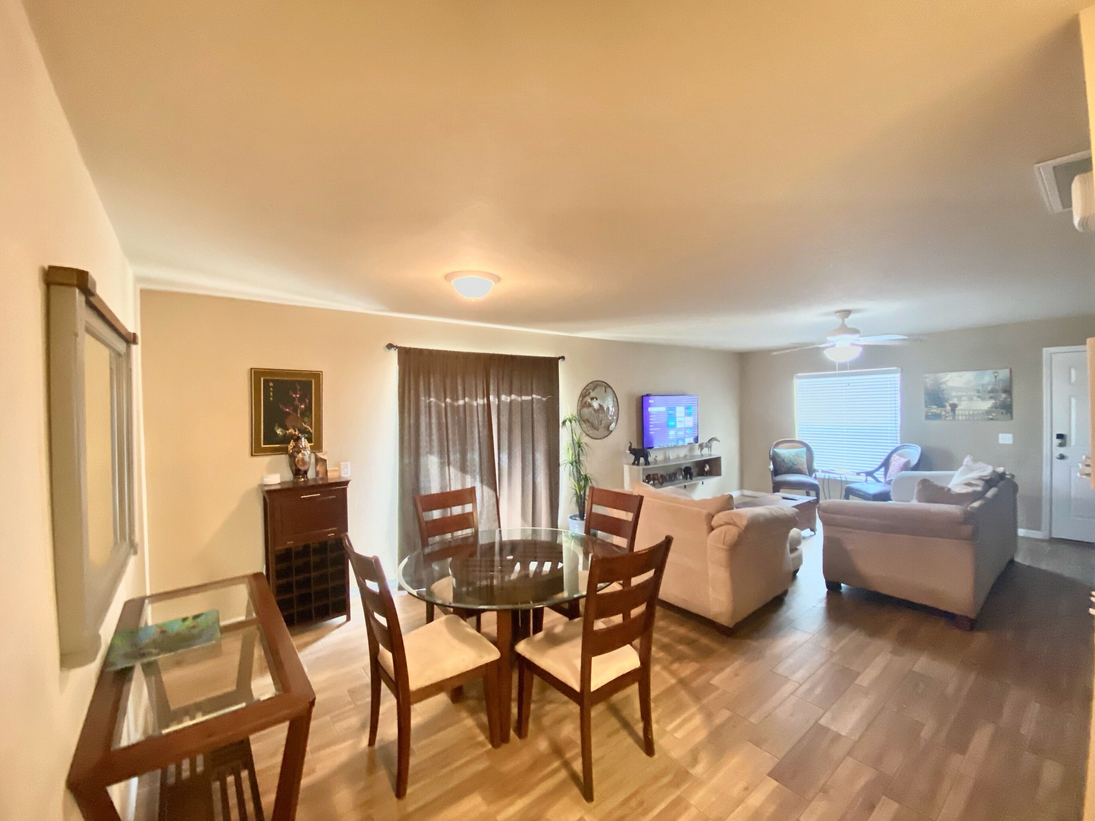 A living room with a glass dining table, wooden chairs, a sofa, and a television.