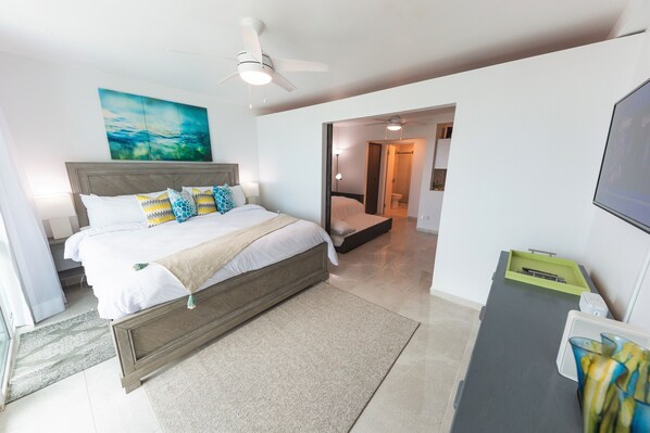 Een moderne hotelkamer met een groot bed, een plafondventilator, een schilderij aan de muur en uitzicht op de badkamer.