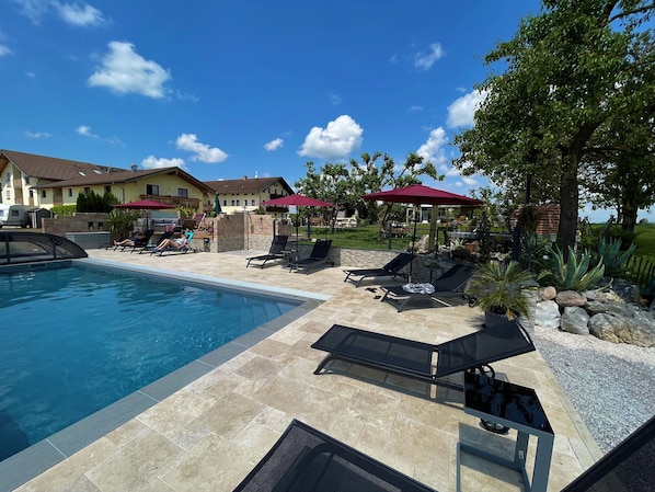 Une piscine entourée de chaises longues et de parasols, un ciel d’un bleu éclatant et une maison en arrière-plan.