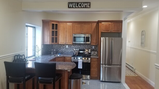 A modern kitchen with wooden cabinets, stainless steel appliances, and a 'WELCOME' sign above the door. - 20-2 Comfortable Quality Cribs (Queens)