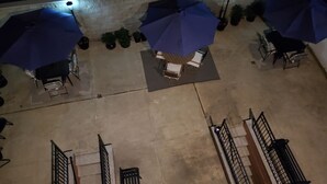 An outdoor patio area with multiple blue umbrellas, a seating area with chairs and a table, and potted plants. - 20-2 Comfortable Quality Cribs (Queens)