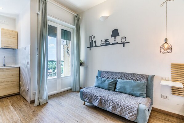 A modern bedroom with a sofa, a wall-mounted shelf with books and a lamp, and a view through a glass door. - Ripa 127 Apartment Navigli (Milano)