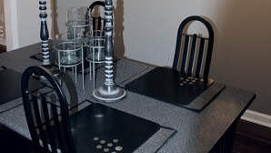 Comedor con mesa negra, cuatro sillas, una araña y un espejo en la pared.