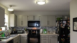 Una cocina con armarios blancos, un microondas negro, un refrigerador negro y un salpicadero de azulejos.