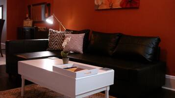 Een woonkamer met een witte salontafel, een zwarte leren bank, een tapijt met een patroon en een schilderij aan de muur.
