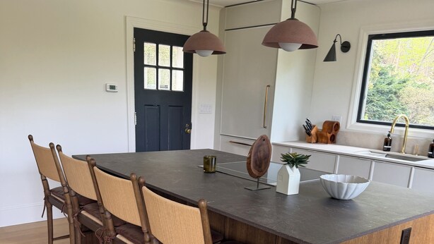 A modern kitchen with a central island, wooden chairs, pendant lights, and a view of the outdoors. - Bear Mountain House. (Philipstown)