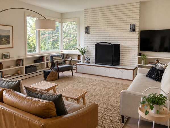 A modern living room with a fireplace, comfortable seating, and a large TV. - Bear Mountain House Near Hiking Trails (Philipstown)