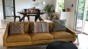 A modern living room with a sofa, ottoman, and dining area. - Bear Mountain House. (Philipstown)
