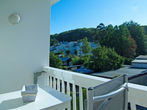En balkon med et hvidt bord og stole, med udsigt over et boligområde med huse og træer.