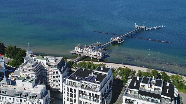 A coastal cityscape with a prominent pier extending into the sea, modern buildings with balconies, and a clear view of the waterfront. - Baltic Building, Apartment 12, Balcony, Elevator, Central Location (Sellin)