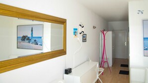 A hotel room with a large mirror, a painting of a lighthouse, a white desk, and a pink chair. - Baltic Building, Apartment 12, Balcony, Elevator, Central Location (Sellin)