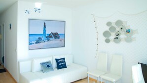 A white room with a painting of a lighthouse, a white sofa with two pillows, and a wall with circular mirrors. - Baltic Building, Apartment 12, Balcony, Elevator, Central Location (Sellin)