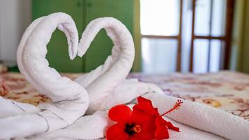 Una cama con una toalla dispuesta en forma de corazón y una flor de hibisco rojo.
