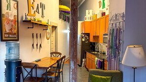 A modern kitchen with wooden cabinets, a dining area with a wooden table and chairs, and a living room with a green armchair and ottoman. - OUR 1B/1B is PERFECT for your NOLA STAY! PARKING Avail! (New Orleans)