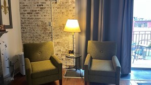 Two armchairs, a floor lamp, and a brick wall in a room with a view of the outside. - OUR 1B/1B is PERFECT for your NOLA STAY! PARKING Avail! (New Orleans)