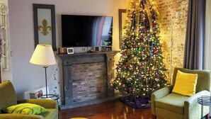 A cozy living room with a brick fireplace, a television mounted above it, and a decorated Christmas tree. - OUR 1B/1B is PERFECT for your NOLA STAY! PARKING Avail! (New Orleans)