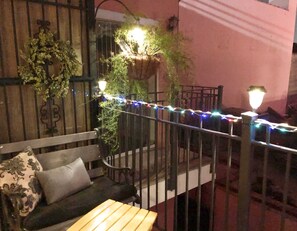 Un balcon avec un banc en bois, une rambarde en métal et des guirlandes lumineuses.