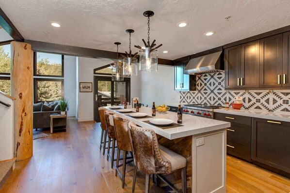 A modern kitchen with a central island, bar stools, dark cabinetry, and a patterned backsplash.