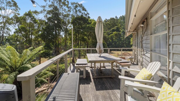 Una terraza de madera con mobiliario exterior, que incluye una mesa y sillas, y un espacio cubierto con una sombrilla.