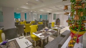 A modern dining area with yellow and grey chairs, white tables, and a decorative plant arrangement. - Pride By Samrat (Jabalpur)