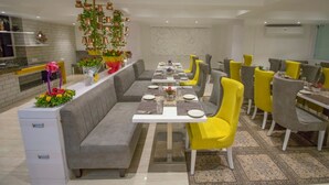 A modern dining area with a long table, cushioned benches, and bright yellow chairs.