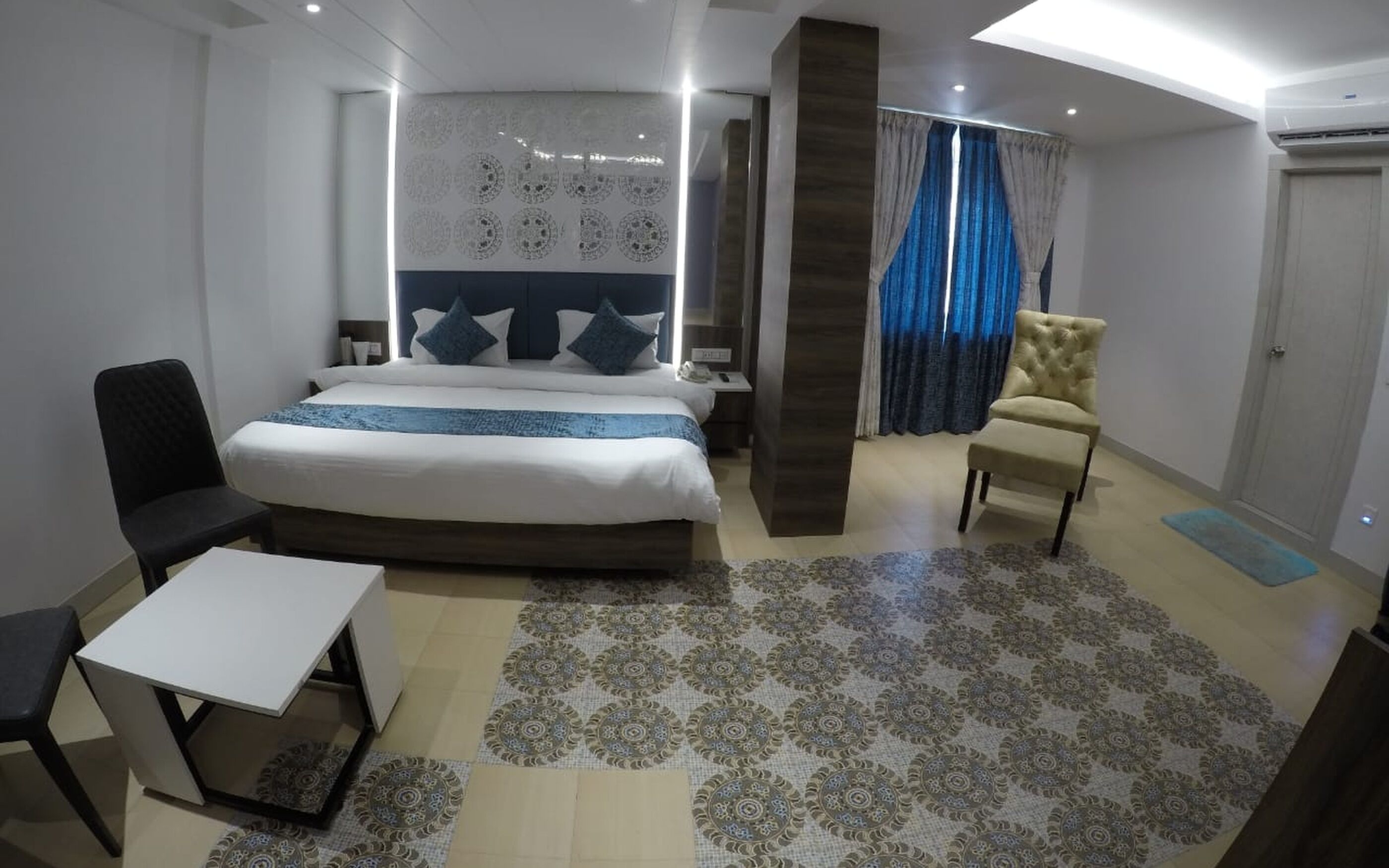 A modern hotel room with a large bed, a desk, a chair, and a decorative wall panel.