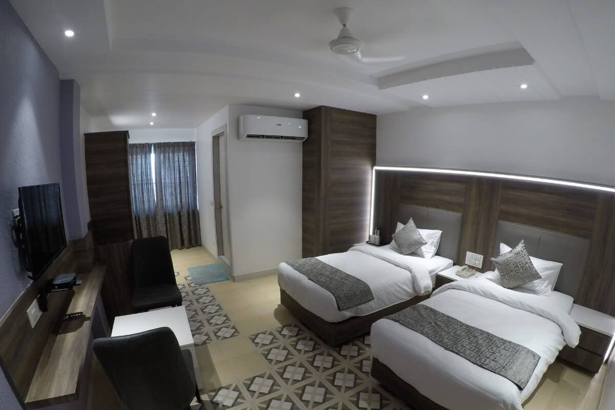 A hotel room with two beds, a desk, a chair, and a TV.