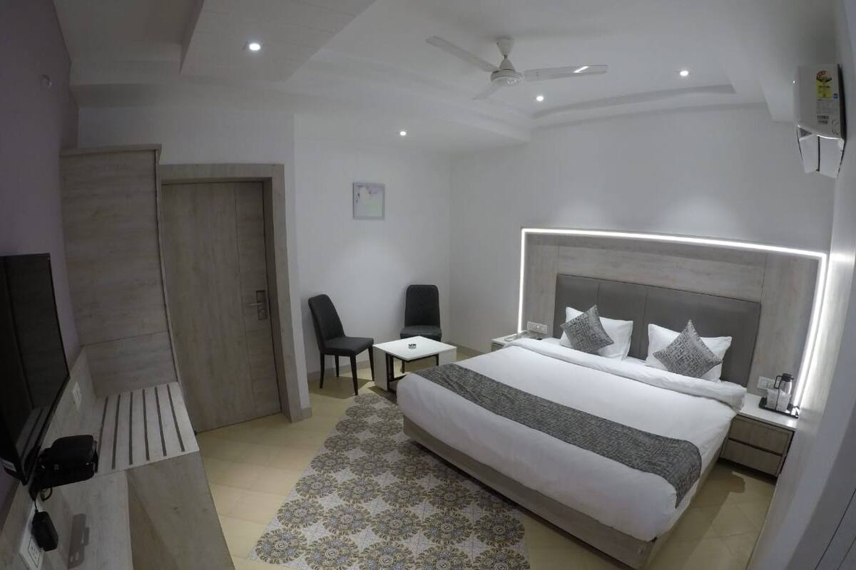 A modern hotel room with a large bed, a desk, a chair, a ceiling fan, and a television.