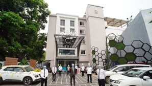 A building with a modern facade, a prominent entrance, and a parking area with several cars. - Pride By Samrat (Jabalpur)
