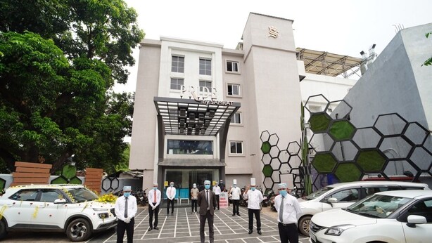A building with a modern facade, a prominent entrance, and a parking area with several cars.