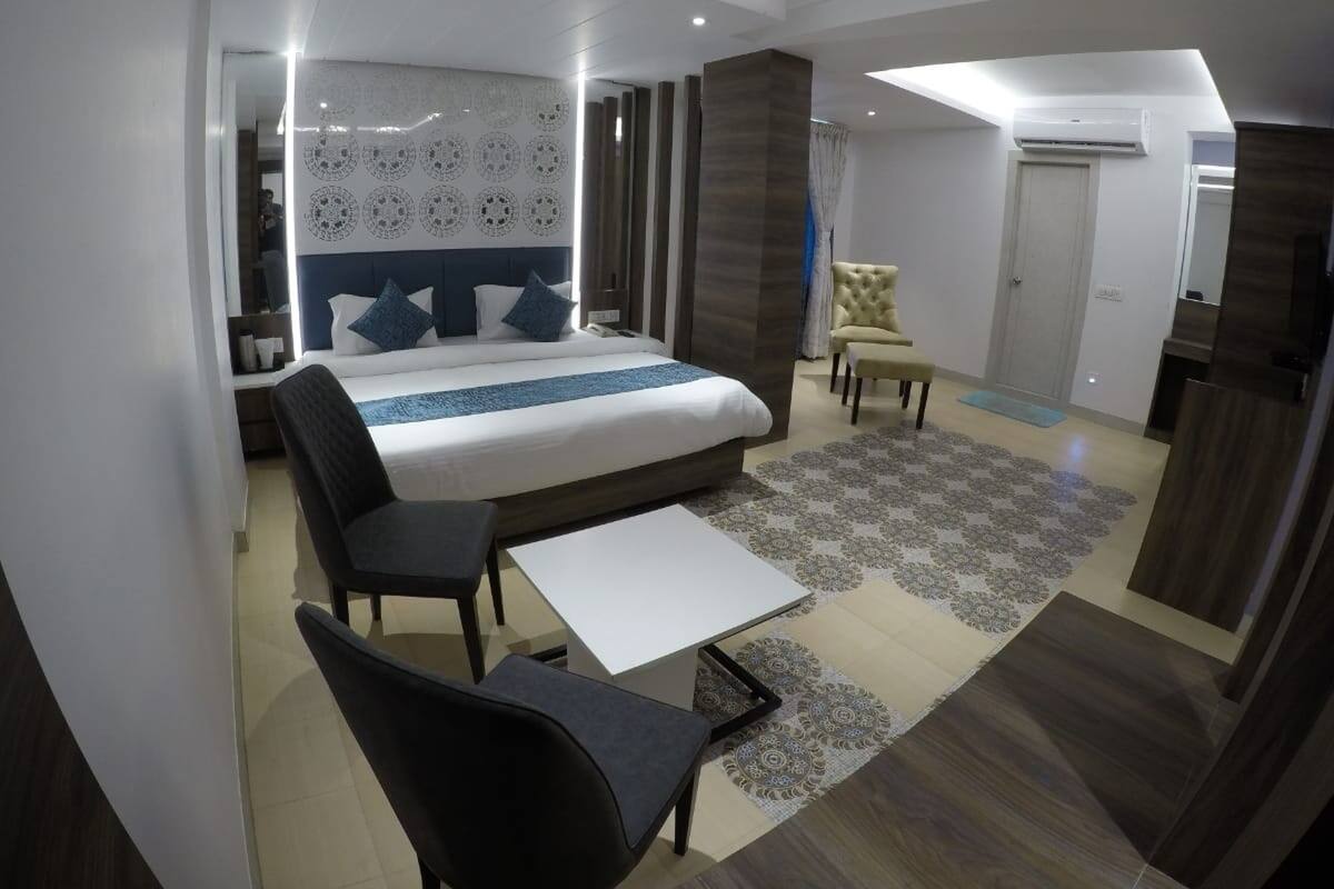 A modern hotel room with a large bed, a desk, a chair, and a small sofa.