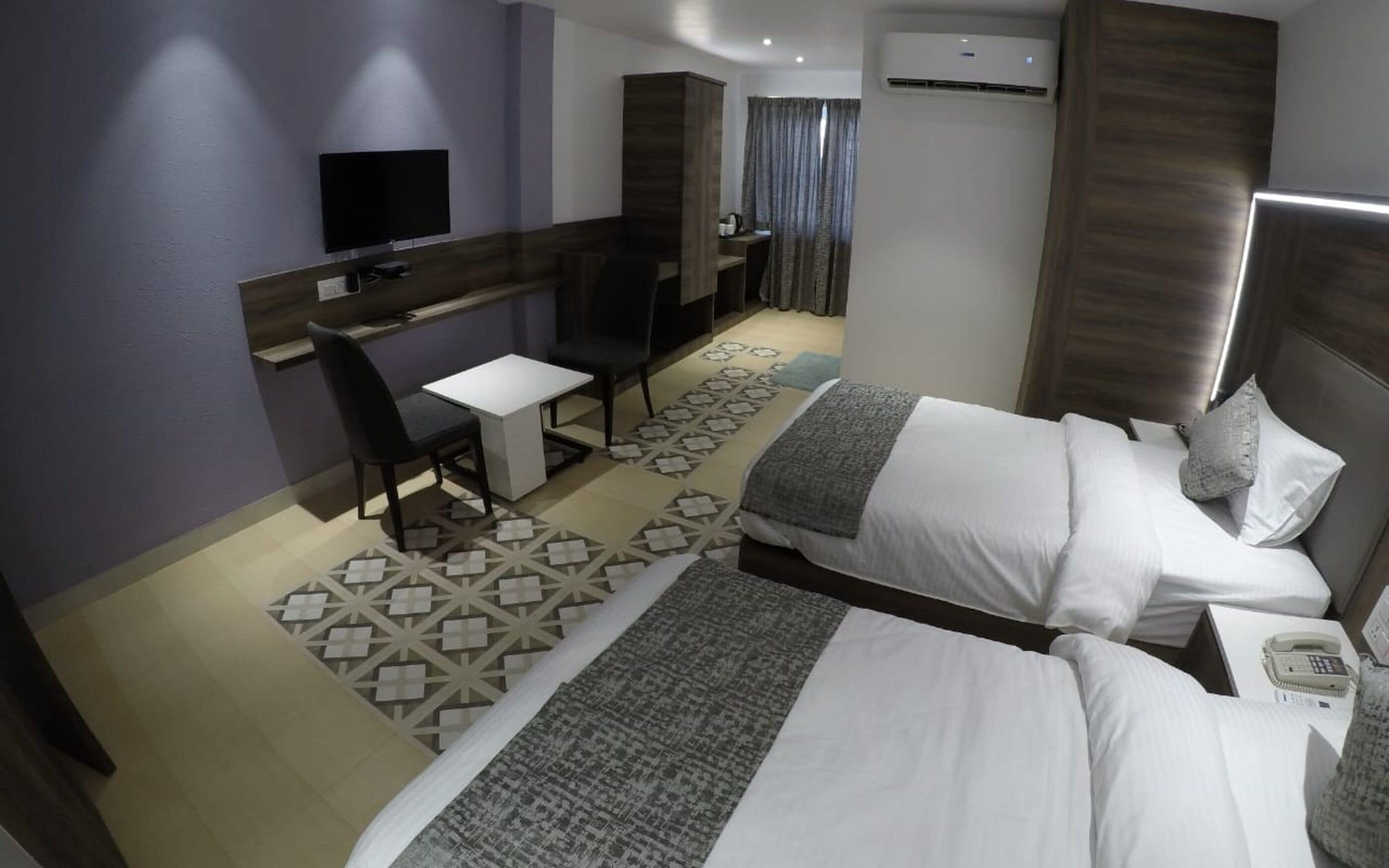 Ett hotellrum med två sängar, ett skrivbord, en stol, en TV och en luftkonditioneringsanläggning.