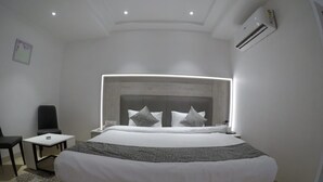A modern hotel room with a large bed, bedside tables, a chair, and an air conditioning unit. - Pride By Samrat (Jabalpur)