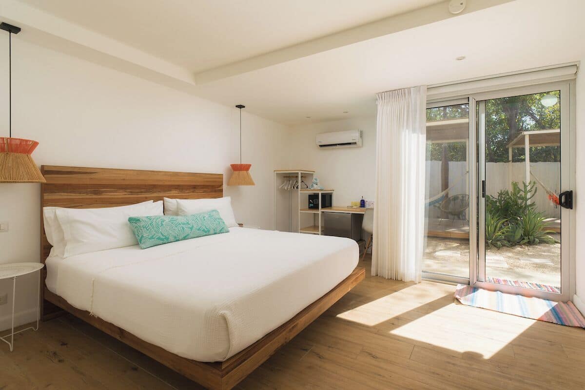 Ein Schlafzimmer mit einem hölzernen Bett, weißer Bettwäsche, einem Schreibtisch und einer Glastür zum Außenbereich.