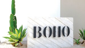 Et skilt med ordet "BOHO" på en marmorbaggrund, omgivet af kaktusser og små planter.