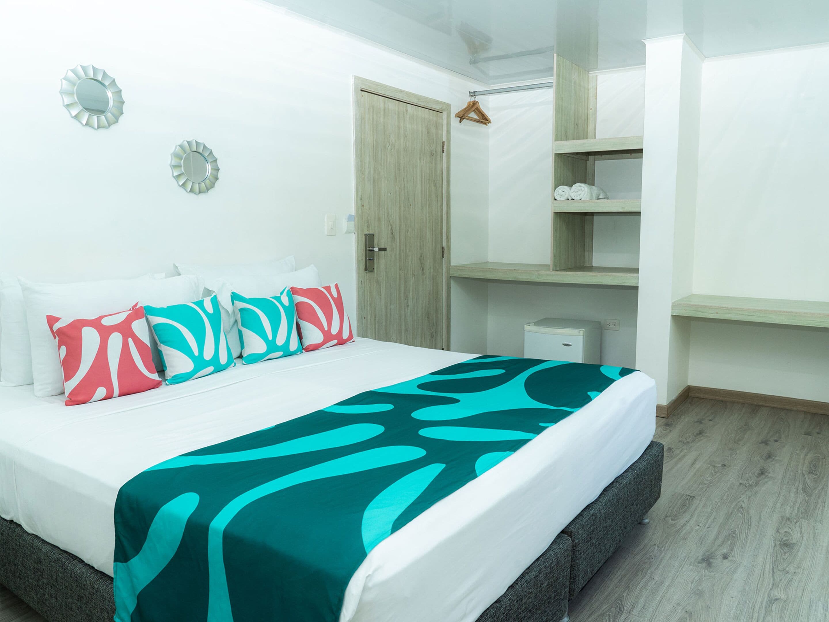 Un dormitorio ordenado con cama, almohadas, una mesita de noche, un armario y una pequeña estantería.