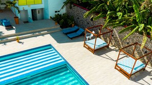 A swimming pool with blue and white stripes, surrounded by lounge chairs with blue cushions and a wooden frame.