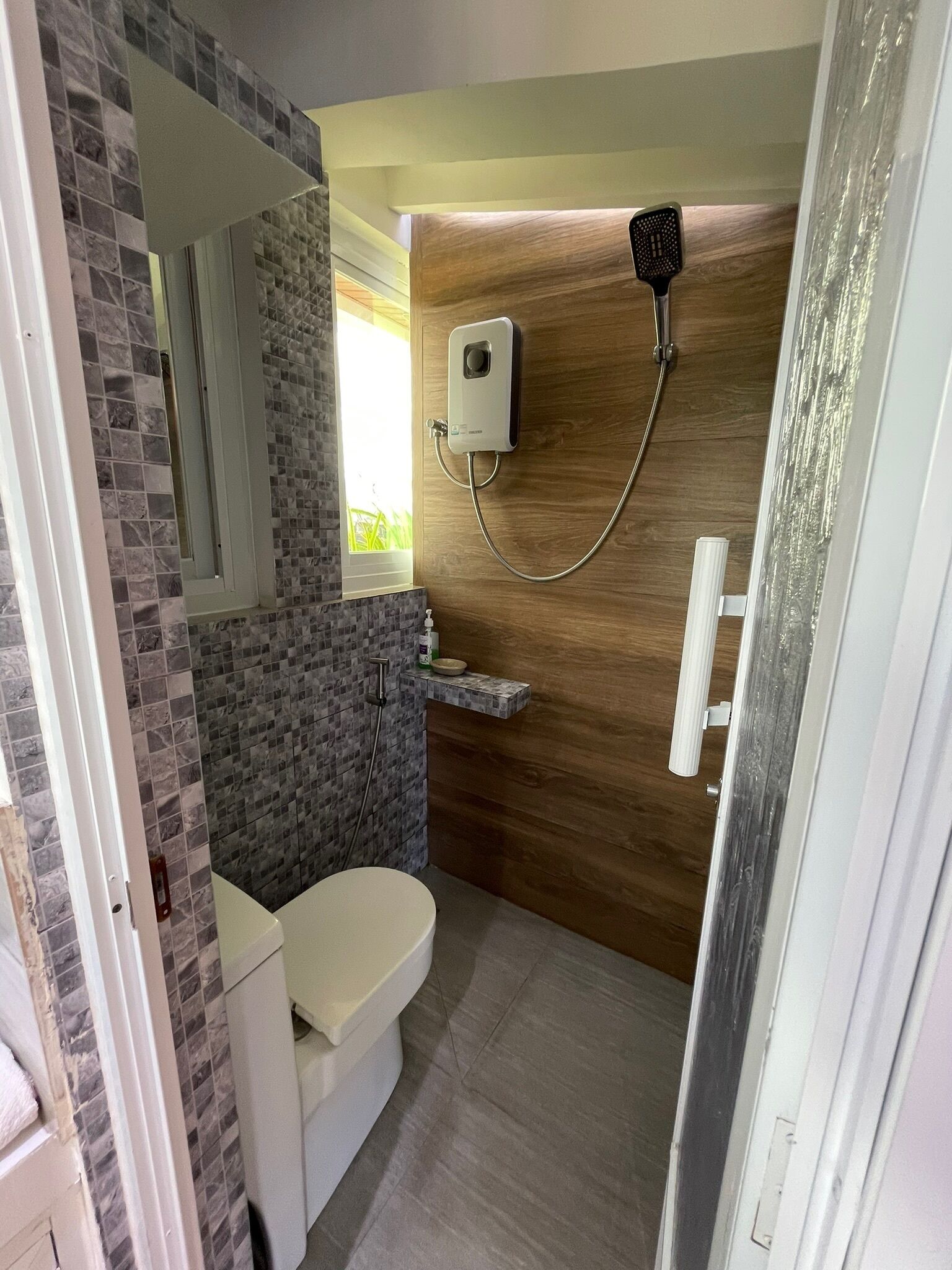 A bathroom with a toilet, a shower, a mirror, and a soap dispenser.