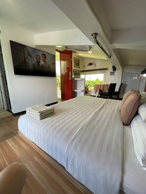 Een hotelkamer met een groot bed, een televisie, een rode deur, een zithoek en uitzicht op groen.