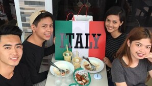 Een groep mensen zit aan een tafel met een groot bord waarop 'ITALY' staat, wat duidt op een eetgelegenheid.