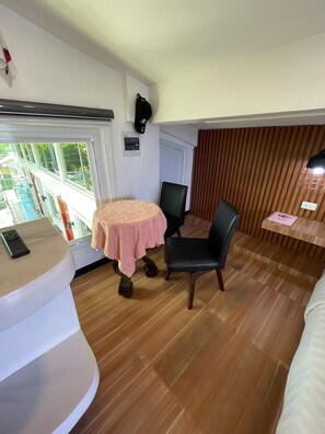 Ein Zimmer mit einem runden Tisch, zwei Stühlen, einem kleinen Schreibtisch mit Telefon, einem Fenster mit Blick und einer Holzwand.
