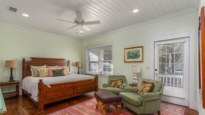 Une chambre à coucher avec un lit en bois, deux tables de chevet, un fauteuil vert, une petite table avec une lampe et un tapis à motifs.