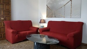 A room with two red sofas, a marble coffee table, a wooden door, and a painting of a bridge. - Alojamiento Rural El Oregano (Campillos)