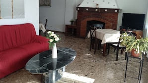 A living room with a red sofa, a marble coffee table, a fireplace, a dining table with chairs, and a TV. - Alojamiento Rural El Oregano (Campillos)